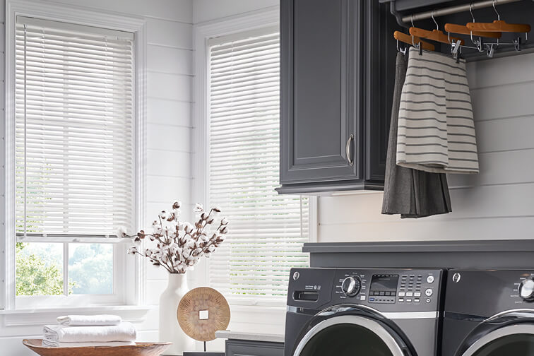 A laundry room with white walls and white blinds covering the windows.