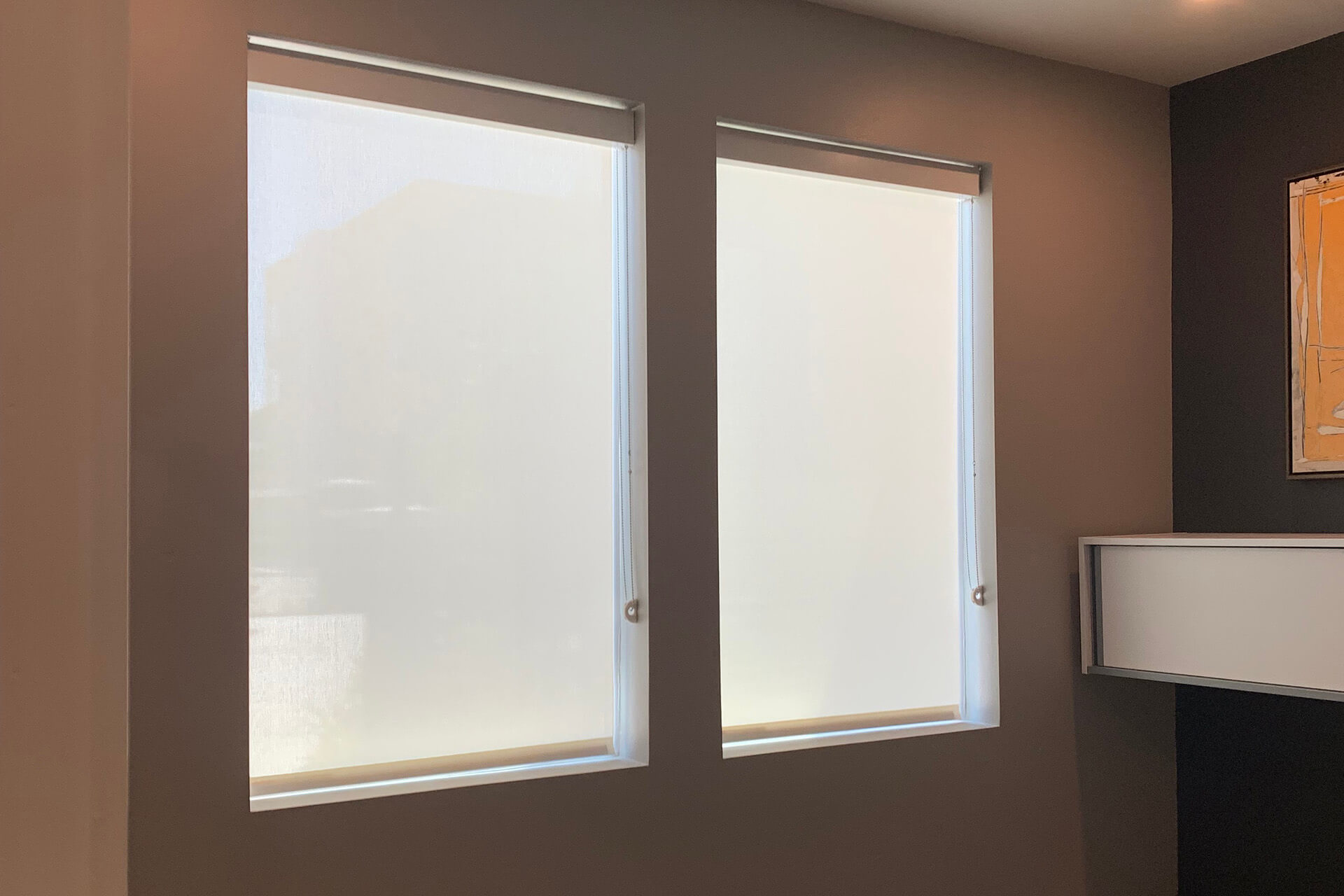 An office room with two windows, each completely covered by roller shades.