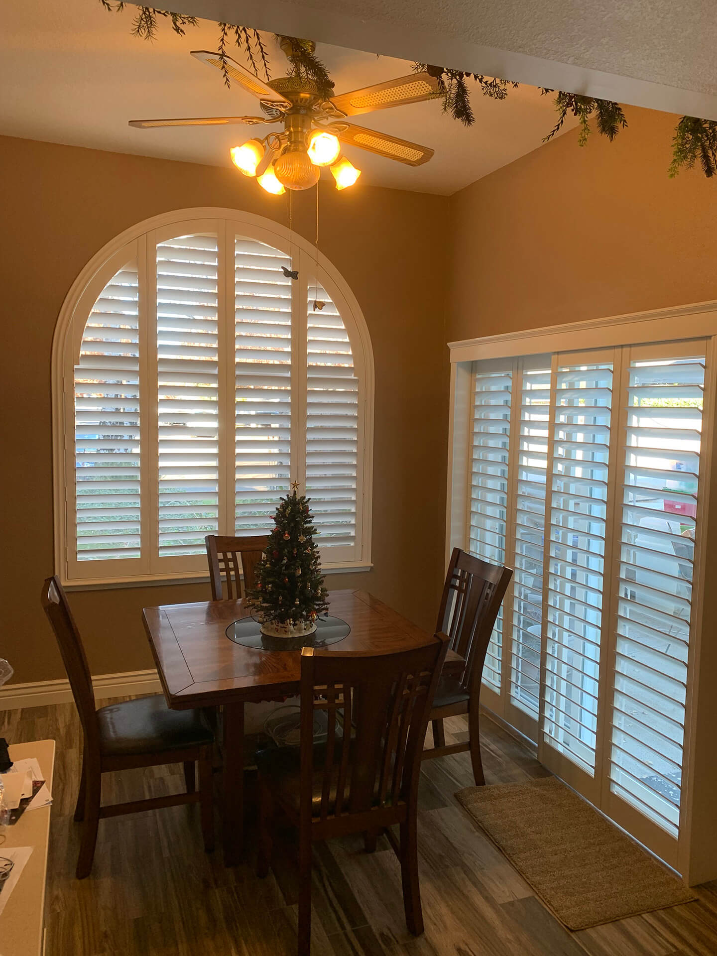 A yellow dining room with shutters coving an arched window and sliding doors.